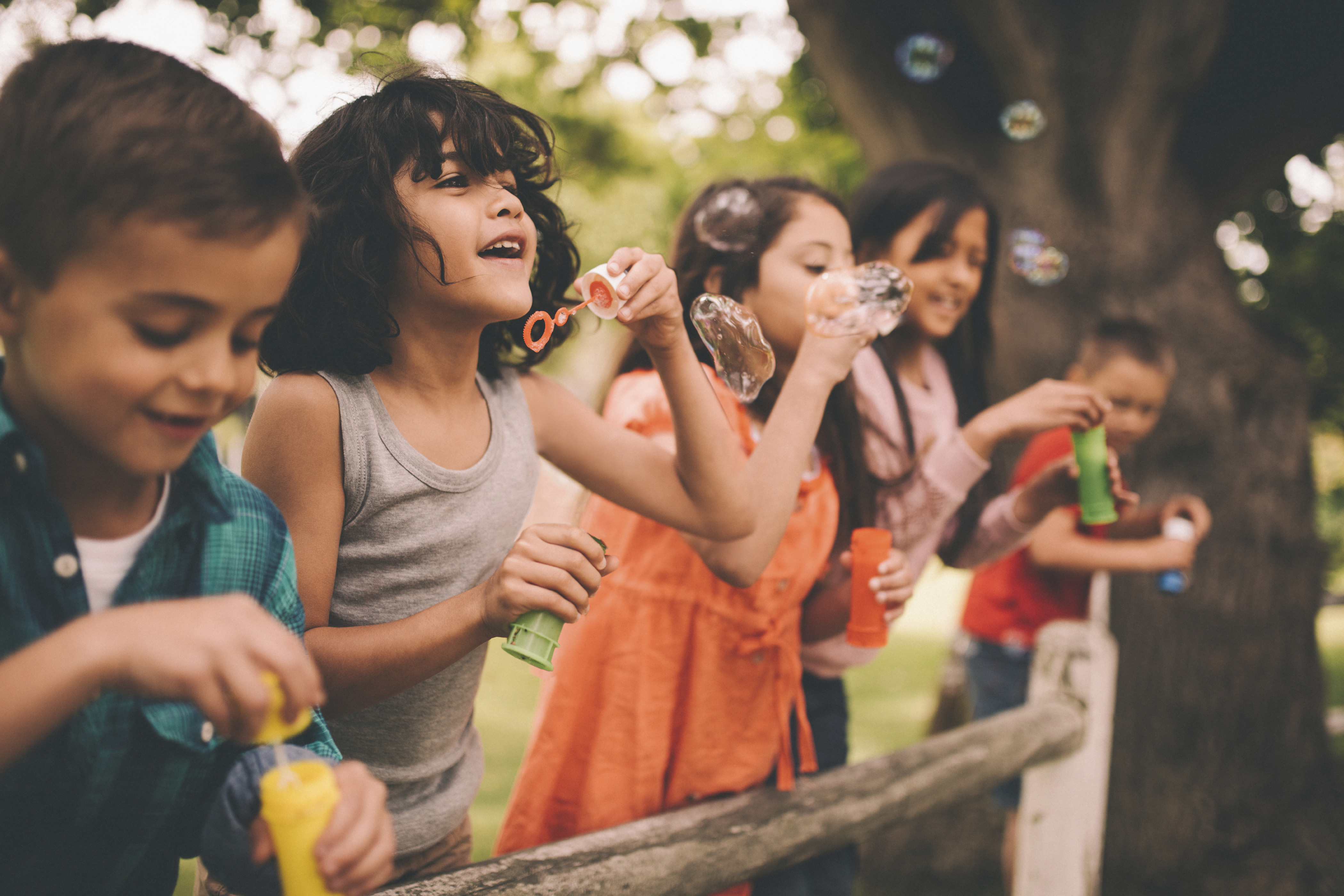 a group of boy and girl children blow bubbles outside