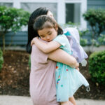 A Korean woman holds her daughter tightly in an embrace, the girl feeling anxious going back to school.