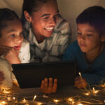 Funny, tablet and mother with children in a tent house streaming internet video, show or movie online in the night. Dark, digital and parent or dad relax with kids watching comedy in the evening