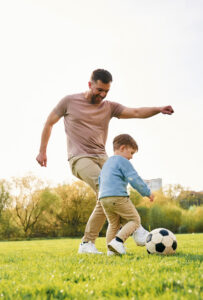 Playing soccer. Happy father with son are having fun on the field at summertime.