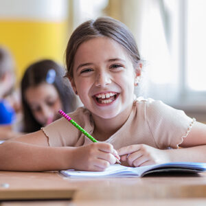 Child smiling while writing in a notebook at school